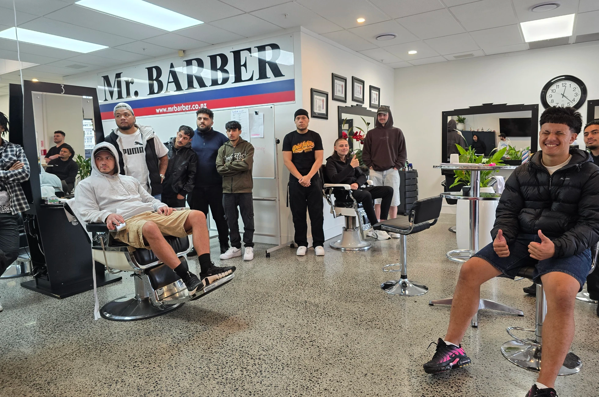 Trainee barbers and clients gathered inside Mr. BARBER Training Centre beneath the shop sign
