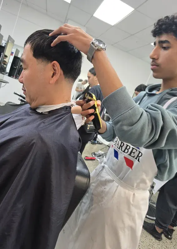 Two barbers, one with a tattooed arm, working closely on a client's haircut