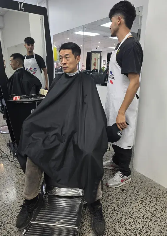 Two barbers working together on a client's haircut at a styling station