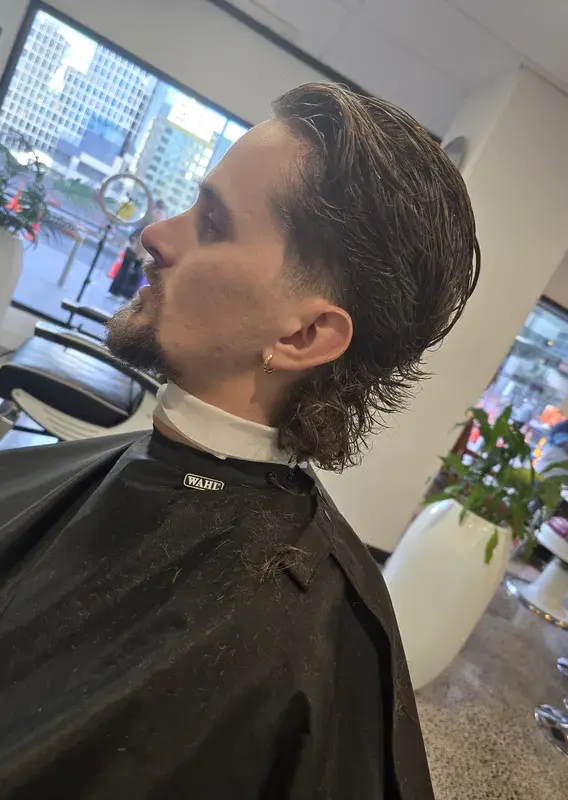 Barber trimming a client's hair beside a red barber chair and striped barber pole