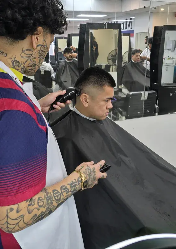 Instructor cutting a client's hair while trainees practice in the background